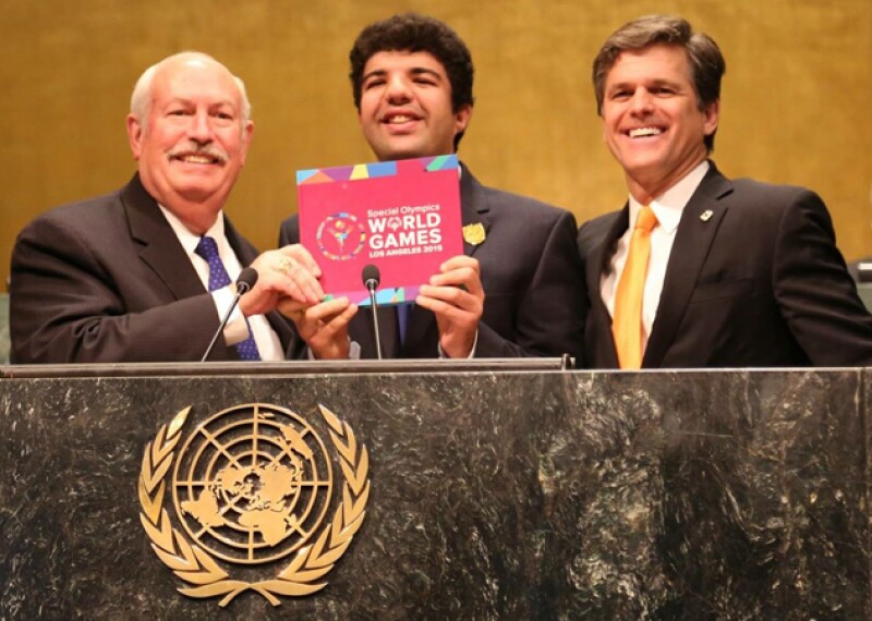 Bob Corlew, Dr. Timothy Shriver, and Special Olympics athlete Mina Baghat standing at a podium at the United Nations. 