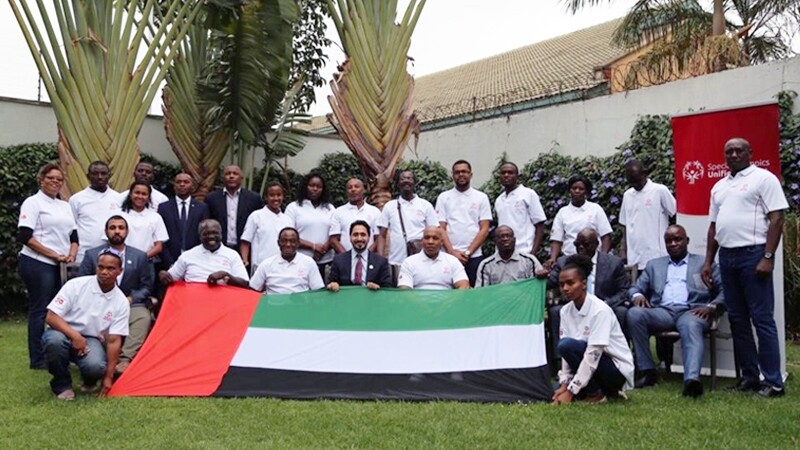 Special Olympics leaders and representatives in a group photo in Africa. A Unified Sports banners is in the background, a country flag is in the foreground.
