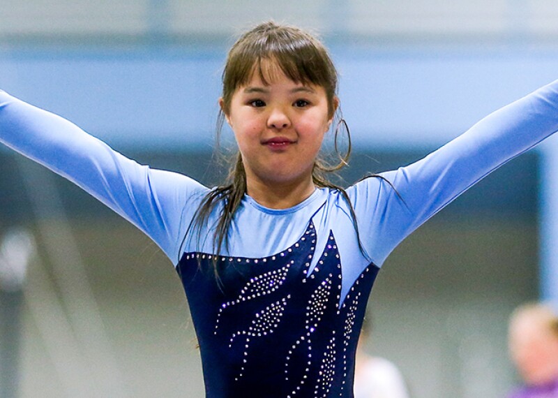 Young girl in a blue leotard raising her arms as she finishes her routine.