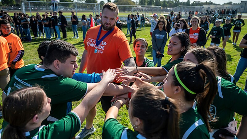 Standing in a circle, a group of students are all in with Dalton Risner.