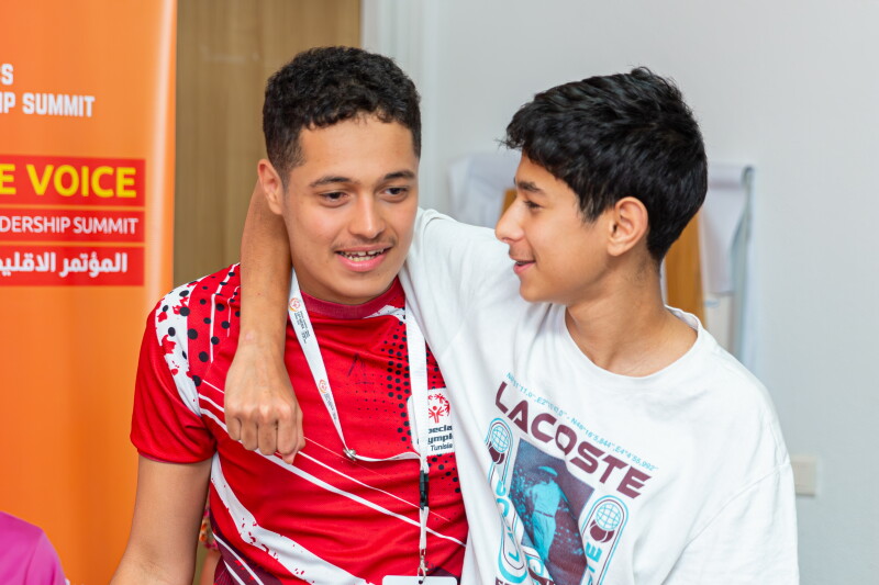 A young boy has his arm around the back of a male athlete's neck, and both are smiling. 