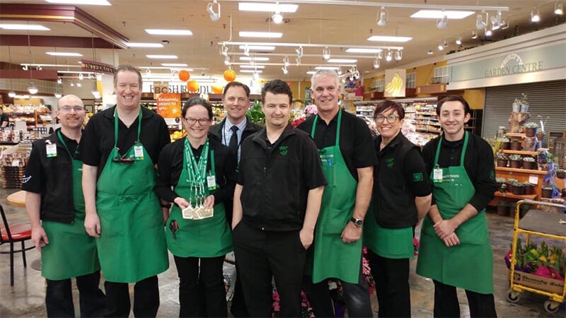 Ashley stands with seven of her coworkers in her store with her medals in hand.