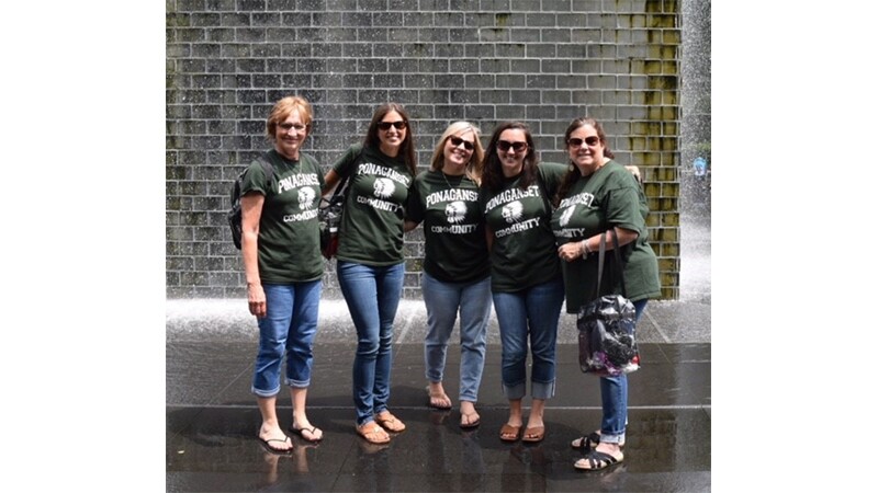 Five teachers wear green Ponaganset shirts and stand in front of fountain.