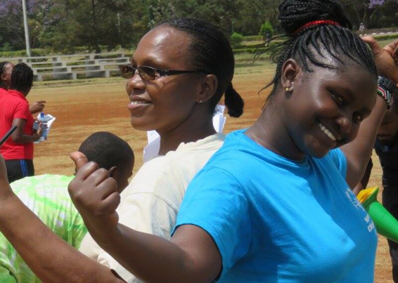 Two female students stand back to back while giving the thumbs up sign.