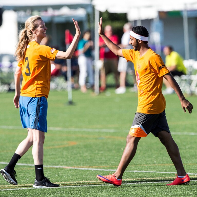 Two players, one male and one female, giving one another a high-5 on the football pitch.