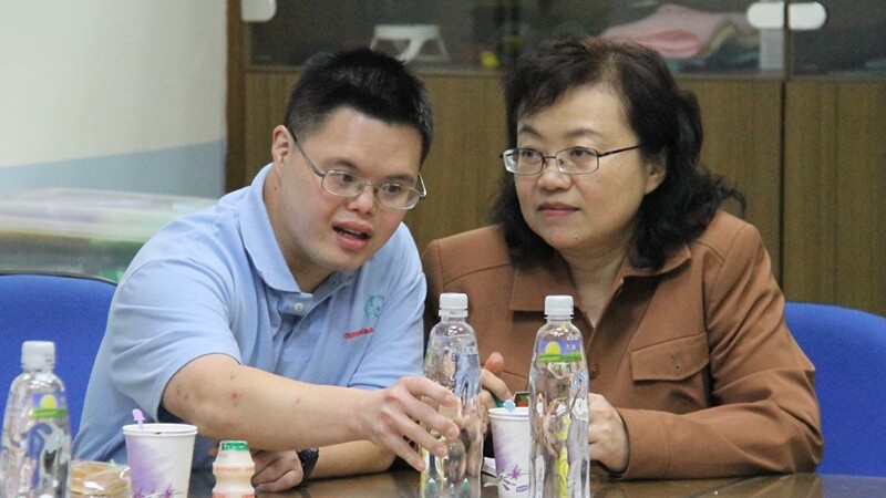 Michael Fan (left) and his mother Angela Huang (right) sitting at a table during a presentation.