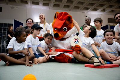 Children sit around a large fox mascot with a row of adults behind them.