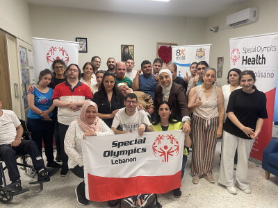 A large group of people holding a flag with the Special Olympics logo smile for a picture.