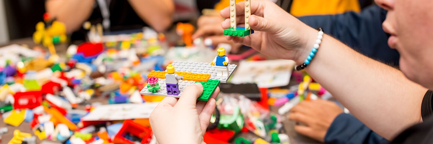Group of people sitting around a table working with "Lego" type blocks.