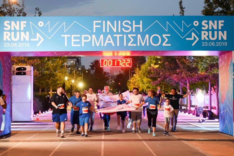 A group of people run towards the camera and across a finish line holding banners and waving their arms in the air.