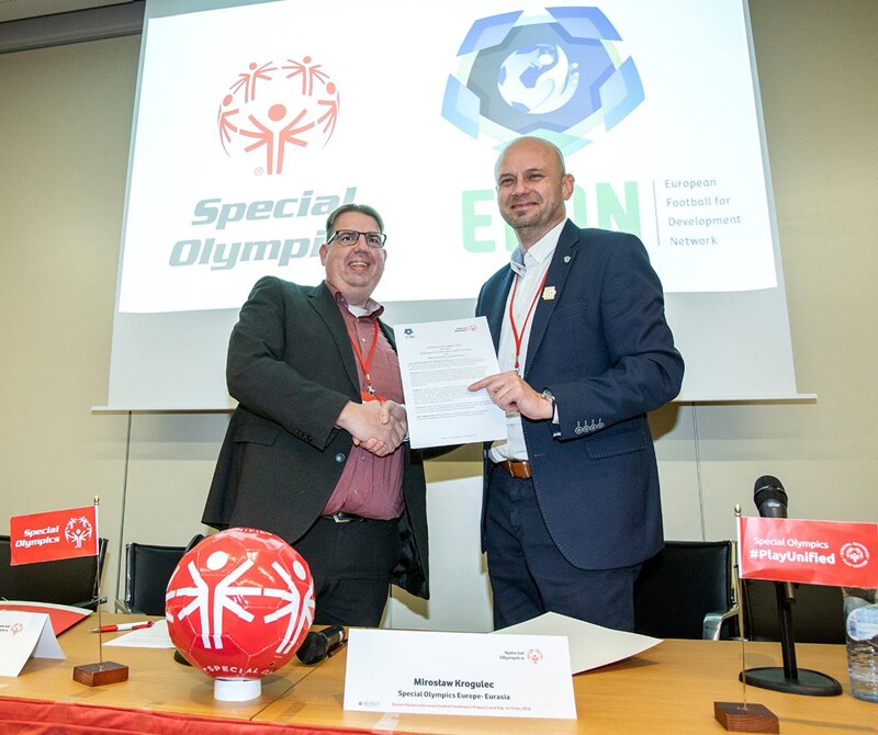 Representatives from Special Olympics and the European Football for Development Network shake hands while on stage holding a contract.