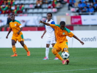 Three players, two from a team in orange and turquoise, one kicking the ball, and the opposing in white and blue.