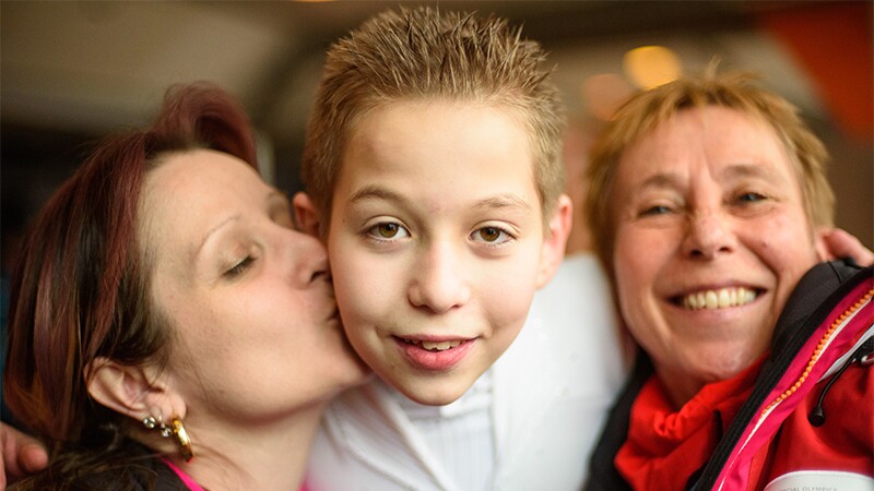 Athlete receiving hugs and kisses from two adult mother figures.