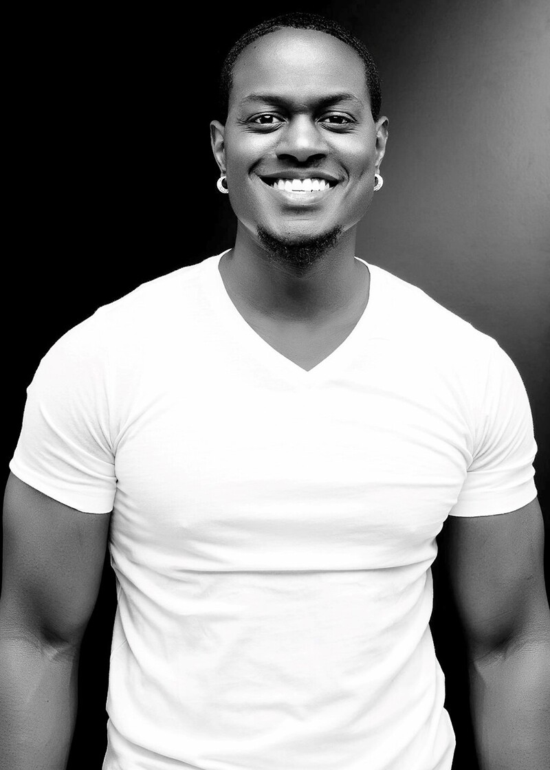 Professional black and white half body shot of Joshua Leonard, in a white t-shirt and a smile.