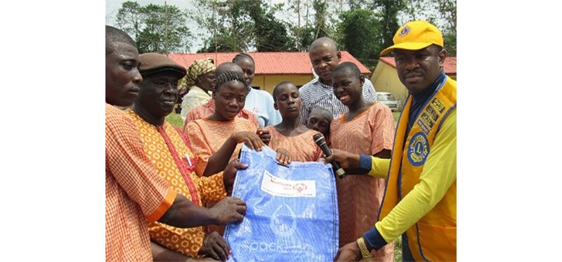 A group and a Lions Club representative (he has a microphone in his hand) and they all together are hold a bag that says "Pack" and has the Special Olympics logo at the top.