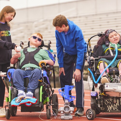 Two people in wheelchair and a person standing next to them. 