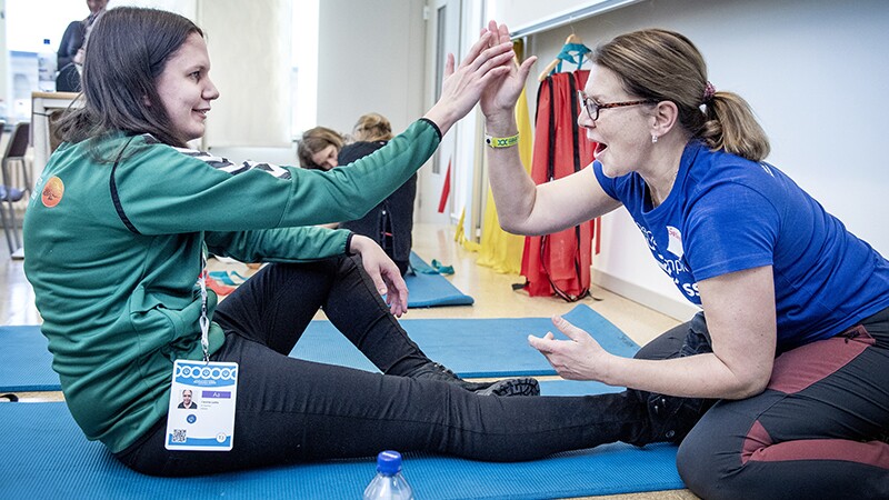 An athlete and volunteer sitting on the ground working on exercises.