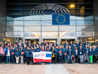 A large group of people stand together with a Special Olympics and European Union branded banner outside a large building.