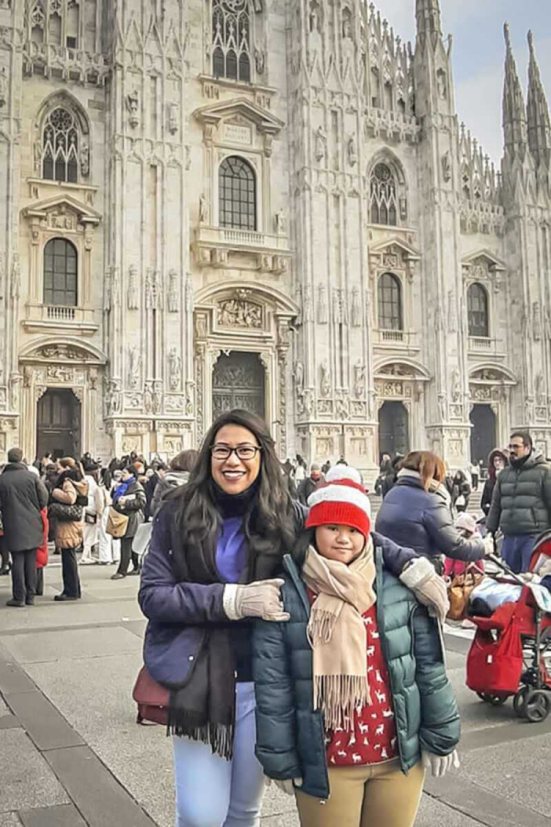 Aloysia and Anastasia standing in front of a Gothic Cathedral, they are both dressed in warm cloths; other patrons visiting the cathedral are seen in the background.