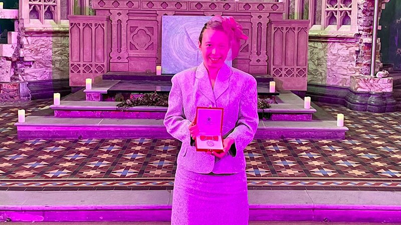 Kiera holding the British Empire Medal and smiling.