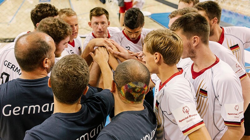 A group of players and coaches standing in a circle with their hands in the middle in a team huddle.