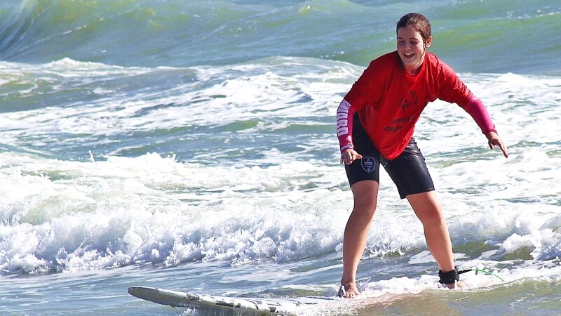 Special Olympics athlete smiles on surfboard in ocean. 