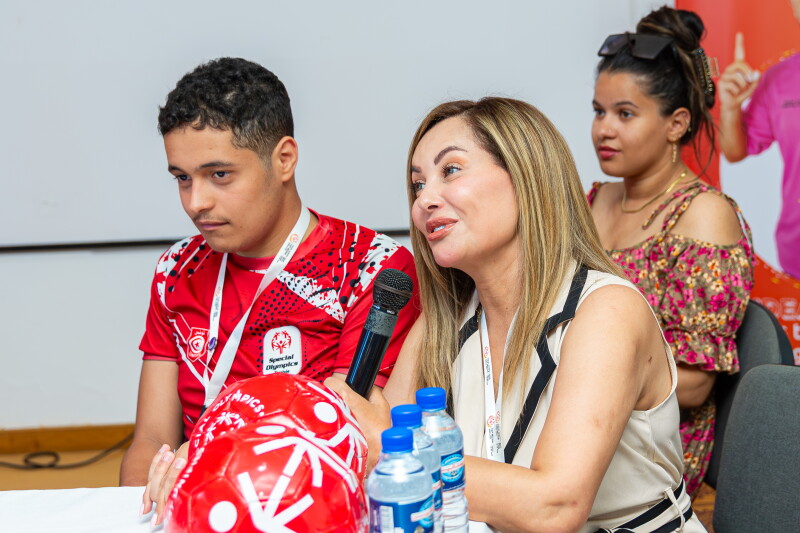 A man and woman sitting at a table. The woman is speaking into a microphone. 