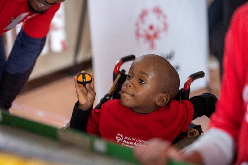 A young athlete in a wheel chair holding a small ball preparing to throw it.