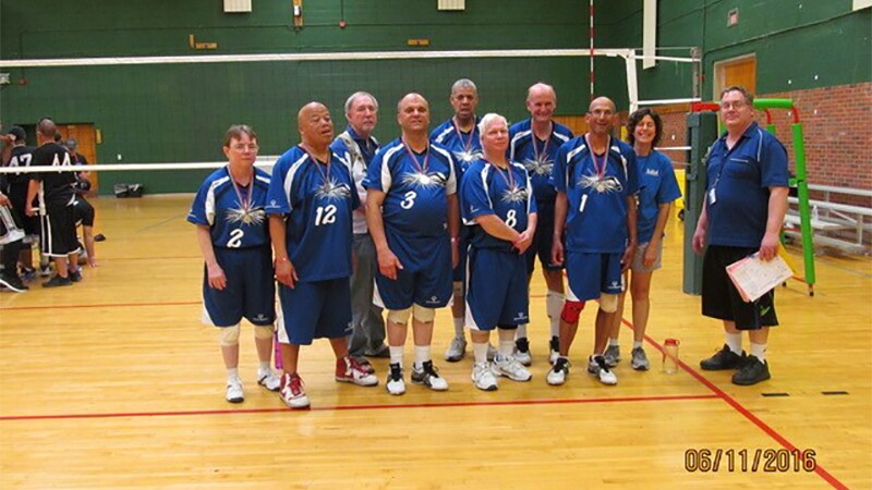 A volleyball team standing on the court and in front of the net for a group photo.