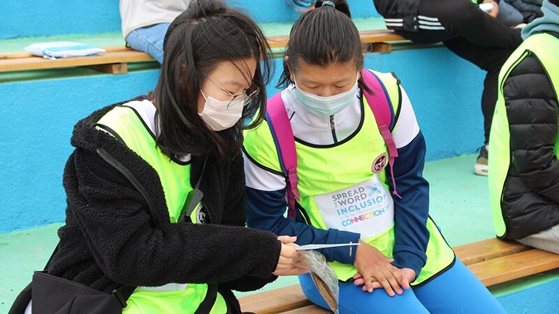 Two young women sitting next to one another on bleachers and talking at a Unified Sports event.