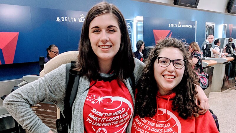 Katie Hut and Natalie Green from SO Utah with their arms around one another at the airport, both have on red Special Olympics t-shirts.