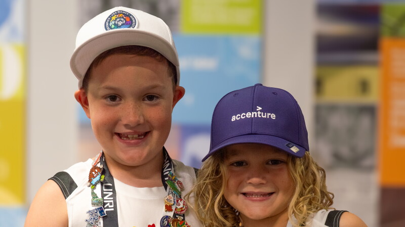 Dos niños pequeños, vestidos con camisetas de los Juegos de Olimpiadas Especiales de EE. UU. y cordones cubiertos de pines coleccionables, sonríen uno al lado del otro, mostrando su creciente colección de pines.
