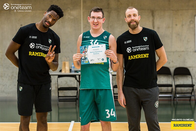 An athlete holding an certificate with other players standing on either side of him in a gymnasium.