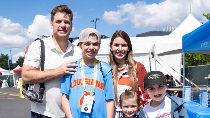 Una familia de cinco miembros sonríe junta al aire libre en los Juegos de Olimpiadas Especiales  de EE. UU., apoyando a su hijo que compite en baloncesto en Minneapolis.