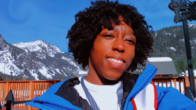 A woman smiles for the camera. She's standing outside in front of mountains. 