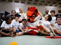 Children sit around a large fox mascot with a row of adults behind them.