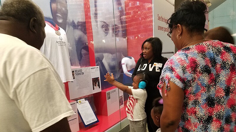 Ricardo Thornton with Seth Rogers at the National Museum of American History's "Morning at the Museum" program. A young child is looking at Ricardo's display with people in the background.