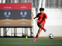 Woman in red kit/uniform kicks ball on football/soccer pitch.