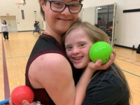 Two athletes share a moment of friendship during a bocce activity, holding bocce balls on an indoor gymnasium court.