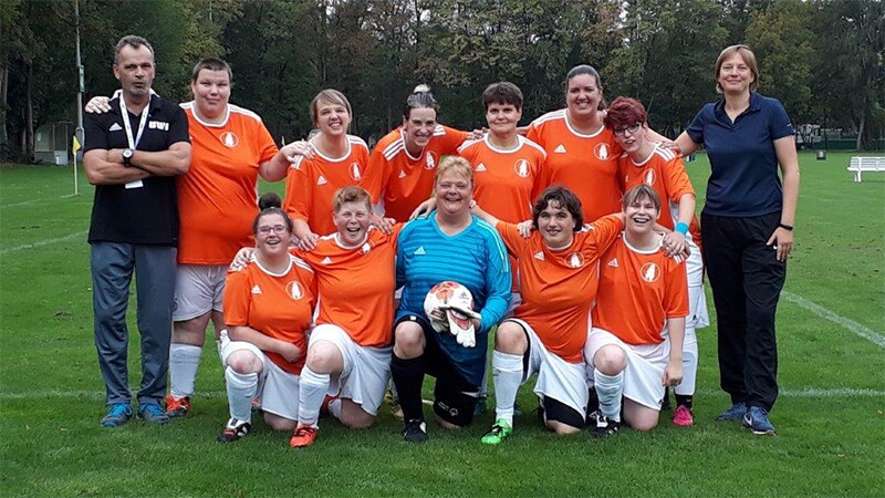 Coach Rob van Someren Brand standing with the Special Olympics women’s football team and another coach on the field for a group photo.