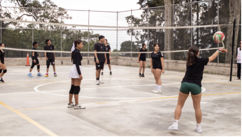 Grupo de jóvenes participando en un partido de voleibol en una cancha al aire libre, en un entorno inclusivo donde se fomenta el trabajo en equipo y la participación. La actividad refleja los valores de Olimpiadas Especiales, promoviendo el deporte unificado y la convivencia entre personas con y sin discapacidad intelectual.
