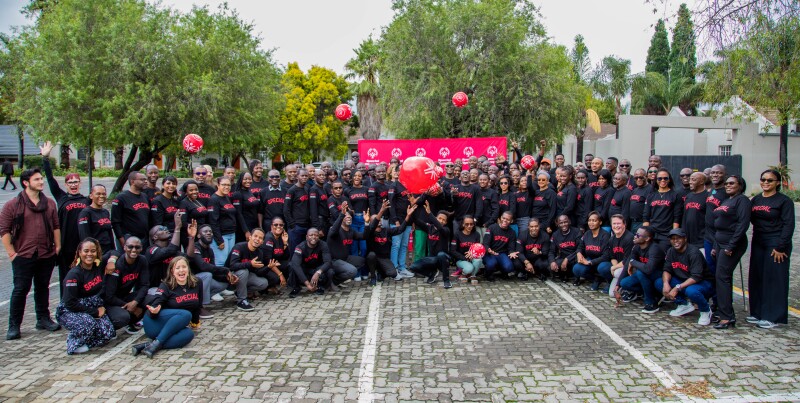 A group of 110 people with black shirts with the text “Special” pose with red footballs, against a red banner with the Special Olympics logo in white.
