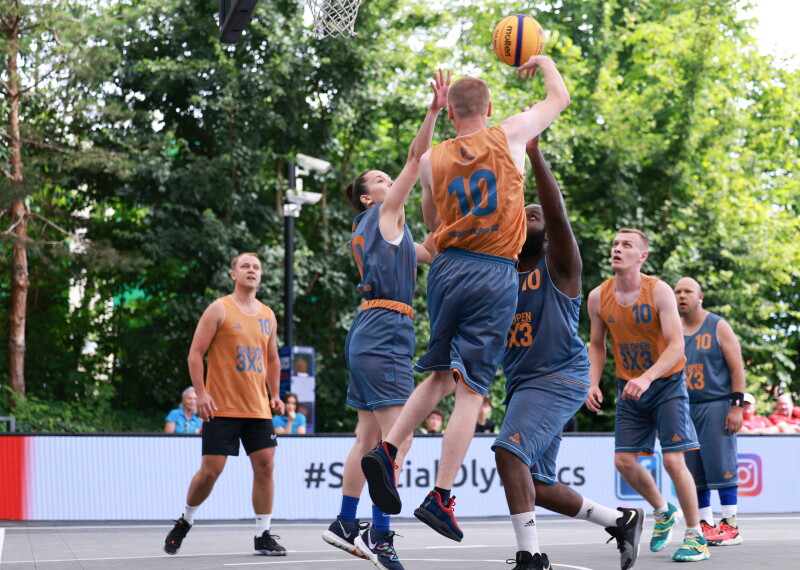 A group of basketball players in grey and orange vie for the ball on a basketball court. 