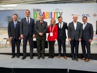 Seven people elegantly dressed, standing and smiling for the camera in front of the stage at the Global Disability Summit in Berlin. 