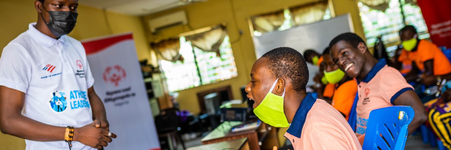 A young man sitting at a desk and asking the class leader a question.