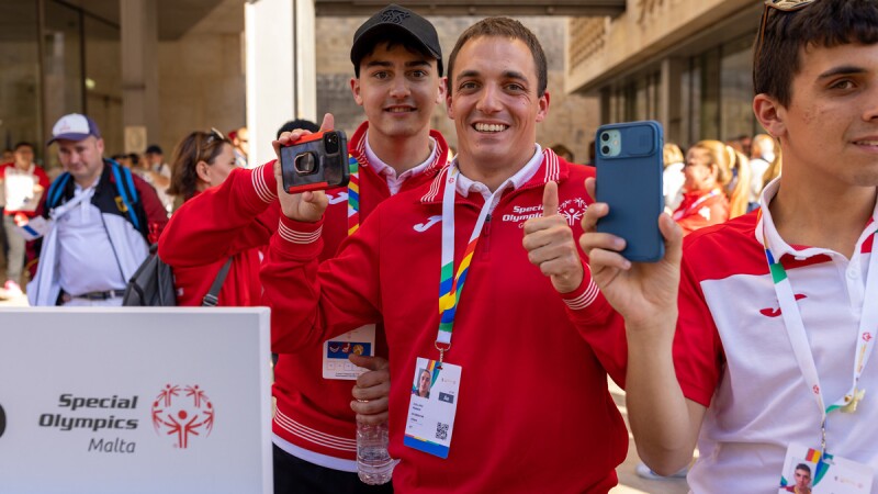 Special Olympics Malta representatives smile for the camera, one holding a camera and giving a thumbs up.