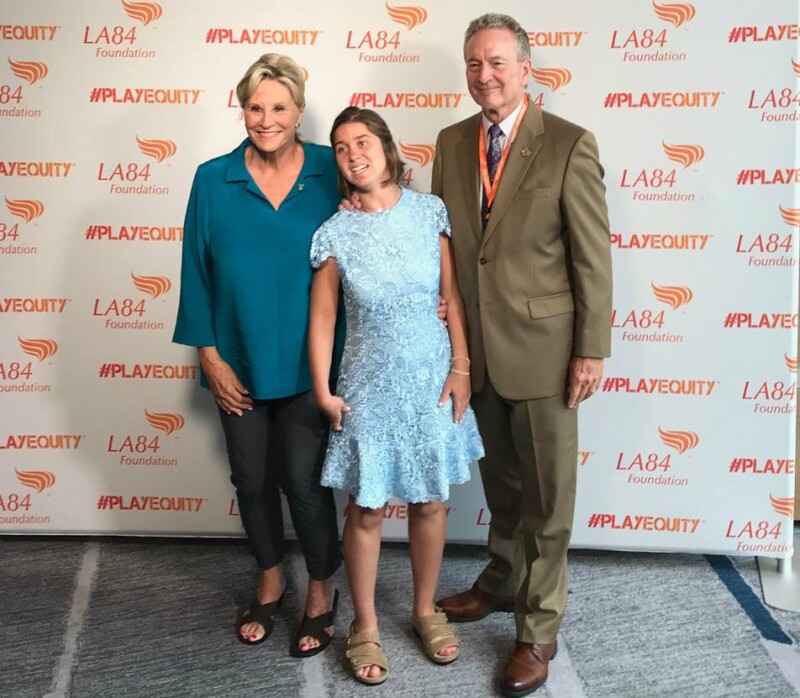 Two women and a man stand together with a branded background smiling at the camera.