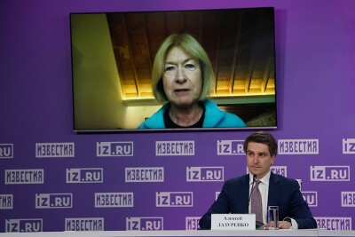 Mary Davis on screen addressing a group of people (out of the image) as a commentator sits and watches. 