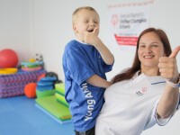 A woman holding a young boy, both smiling and giving a thumbs up
