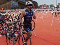 an athlete in a blue camouflage uniform and a bike helmet walks alongside his bicycle